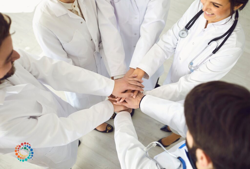 View looking down on five physicians with hands reaching into center of a circle symbolizing consensus