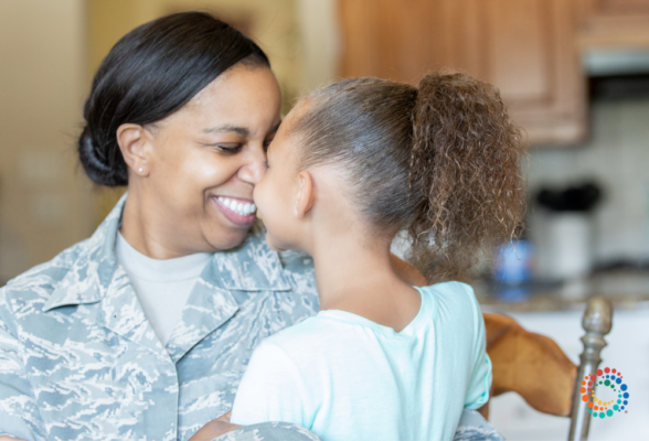 A mother in a military uniform smiling and holding her daughter