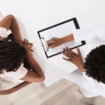 An african american doctor sitting with patient going over papers on a clip board used to portray a doctor taking the time to really learn and understand the patient