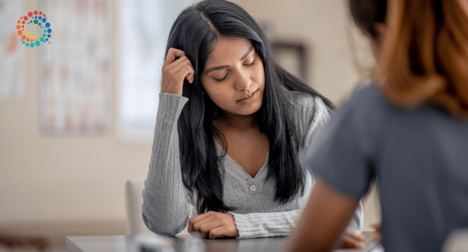 Woman with long black hair leaning her head on her hand looking down. Picture is used to depict "mental health" struggles