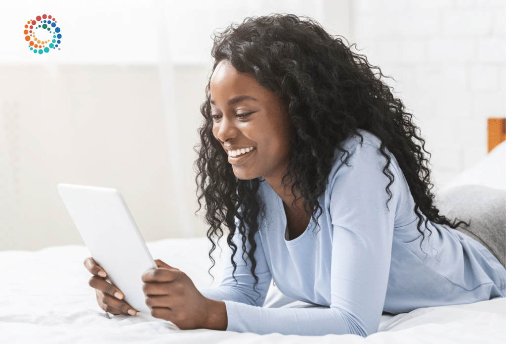 African amercian woman laying on her stomach looking at a tablet smiling and reading what is on the screen